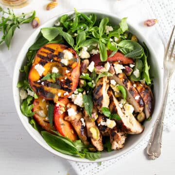 grilled peach and chicken salad with arugula in a bowl.