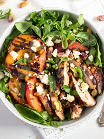 grilled peach and chicken salad with arugula in a bowl.