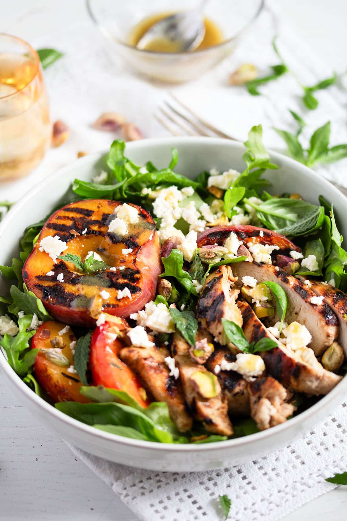 large bowl with arugula salad topped with grilled peaches and sliced chicken.