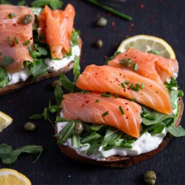 smoked salmon sandwich with capers and lemon wedges.