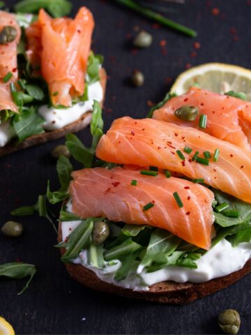 smoked salmon sandwich with capers and lemon wedges.