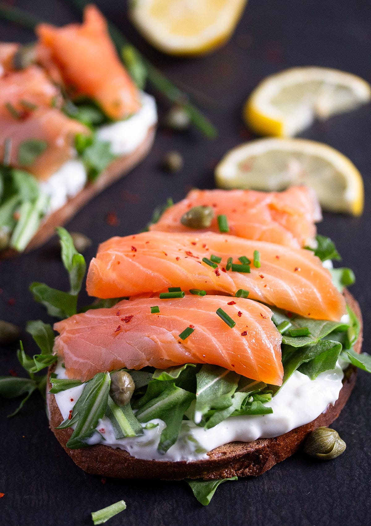 close up of sandwich with cream cheese, arugula and three smoked salmon slices on top.