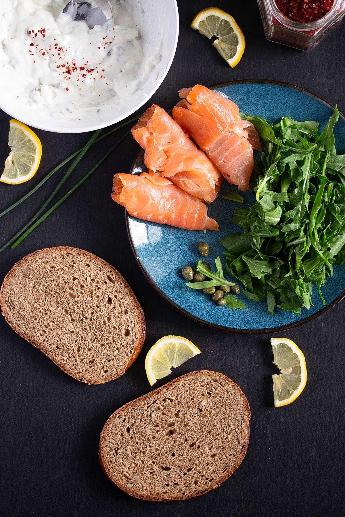 ingredients for sandwich with salmon, arugula, bread, cream cheese and capers.