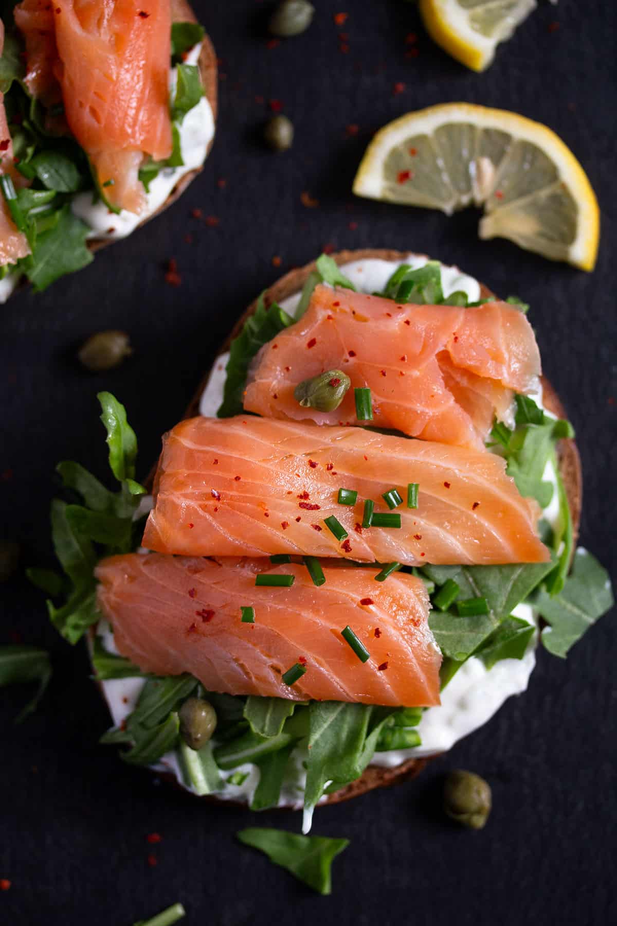 one open faced salmon sandwich with arugula and lemon wedges beside it. 