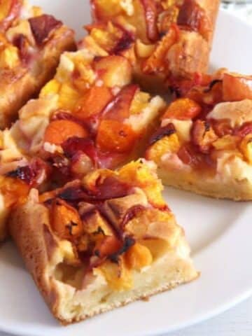 many squares of sour cream peach cake on a plate.