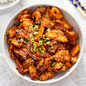 gochujang chicken breast sprinkled with sesame seeds and green onions in a bowl.