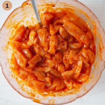 mixing raw chicken breast pieces with gochujang sauce in a bowl.