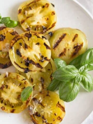 many slices of charred grilled green tomatoes with basil on a plate.