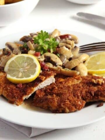 german schnitzel with mushrooms sauce and lemon slices on a plate.
