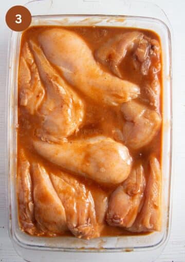 chicken breast pieces marinating in sauce in a large glass baking dish.