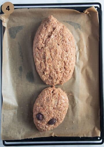 uncooked meatloaf shaped as a spider with large body, smaller head and olives eyes.