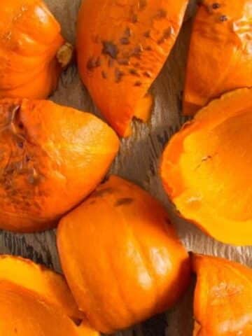 many roasted pumpkin halves on a baking sheed lined with brown parchment paper.