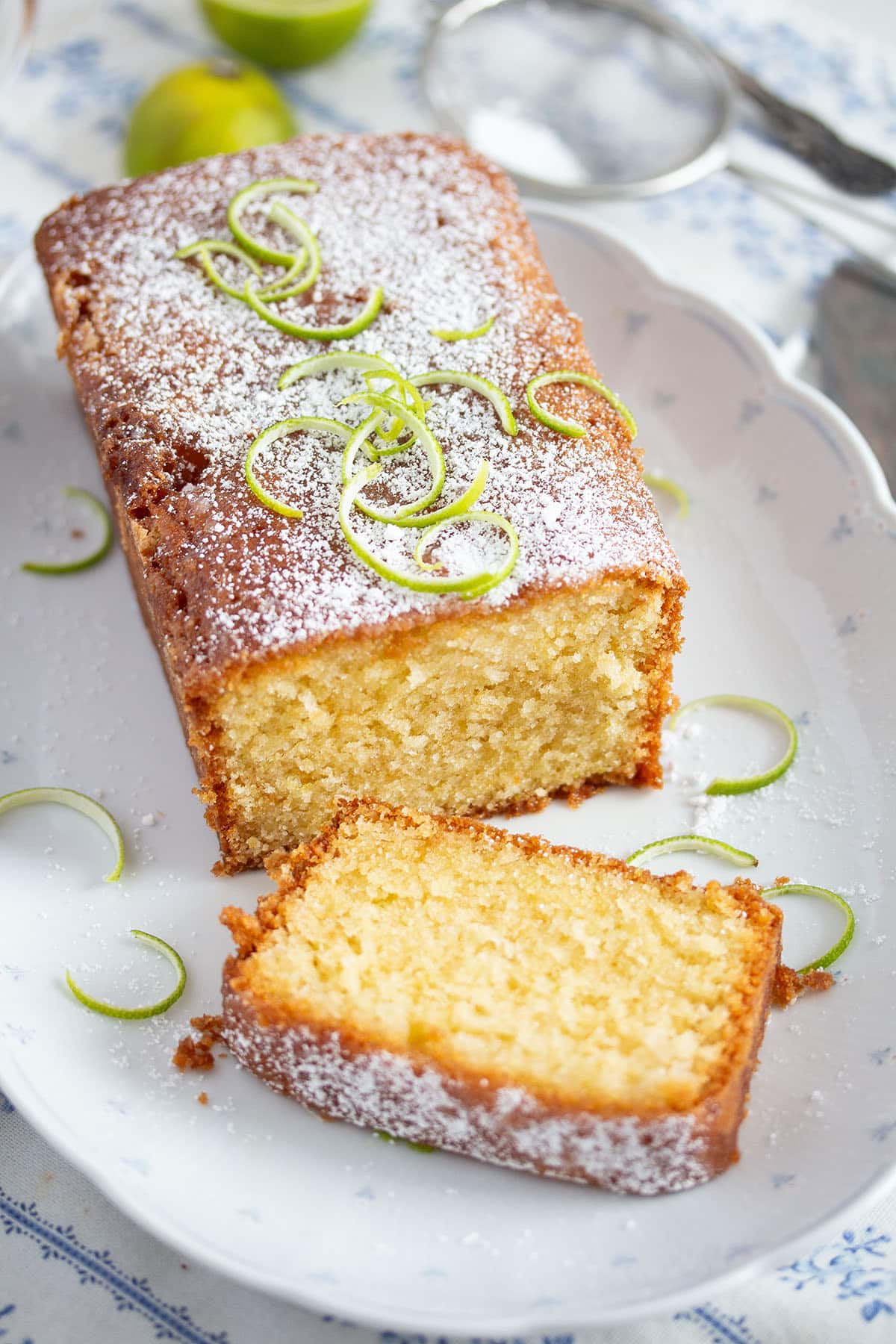 loaf of lime cake with lime drizzle sliced on a platter.