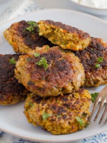 many golden brown oatmeal patties stapled on a plate with a fork.