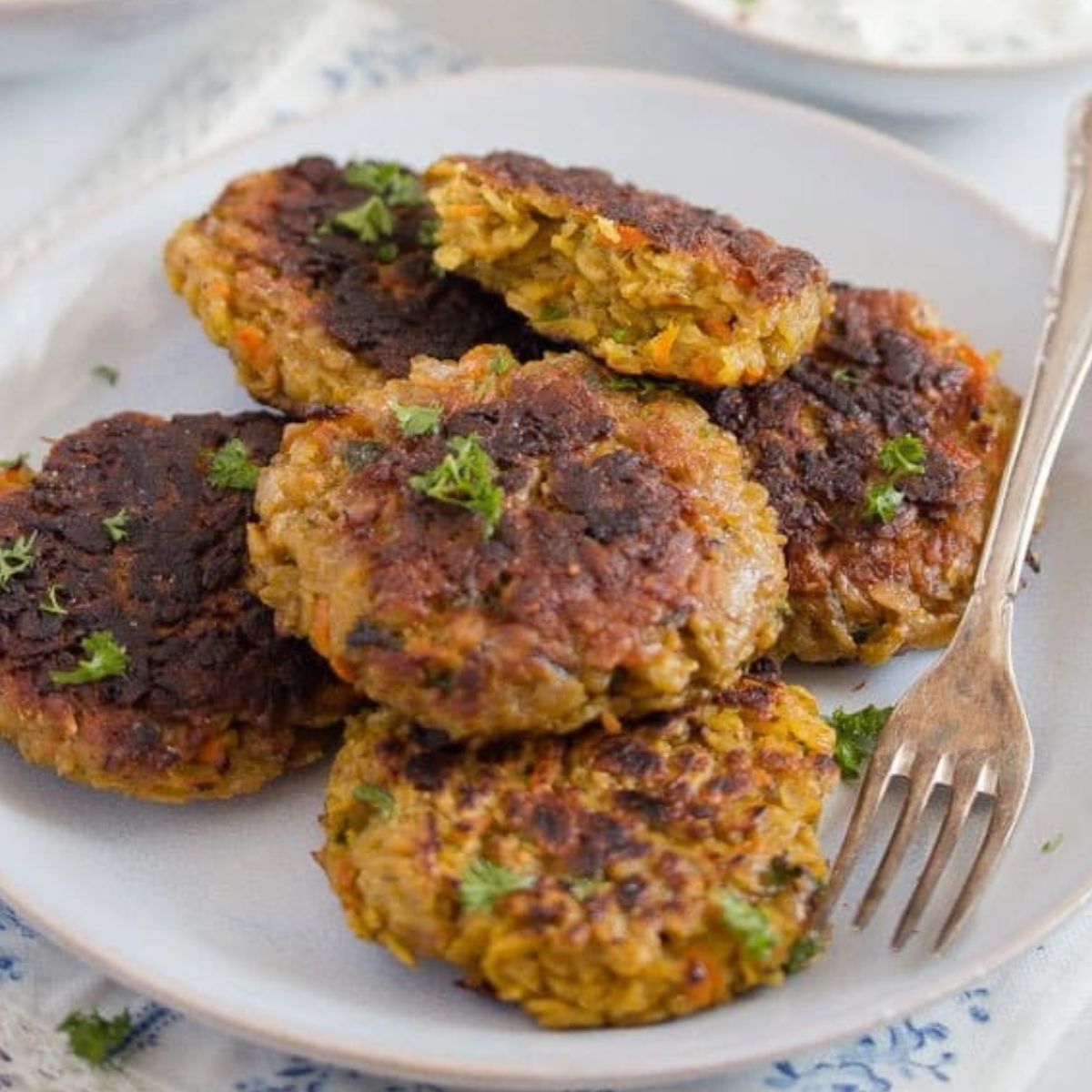 many golden brown oatmeal patties stapled on a plate with a fork.