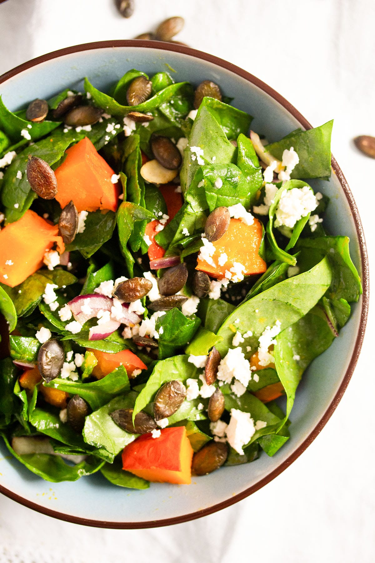close up of a bowl with spinach, pumpkin salad with feta and pepitas.
