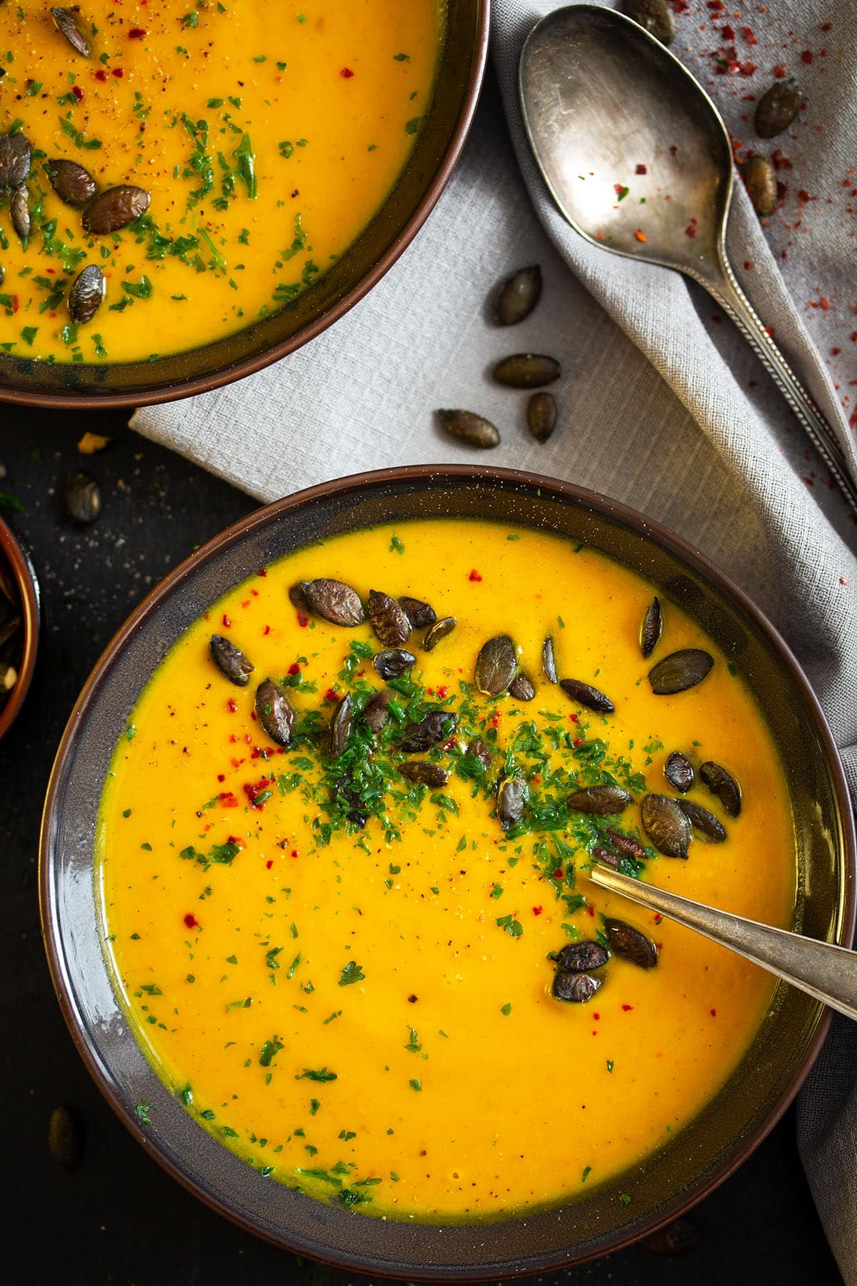 two bowls with roast pumpkin soup garnished with seeds and parsley.