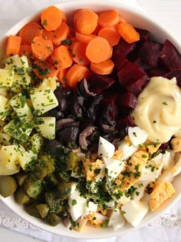 salade russe with potatoes, carrots, beets, eggs and mustard in a bowl.