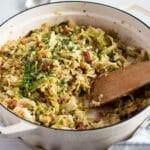 sauteed savoy cabbage with bacon in a large dutch oven with a wooden spoon in it.