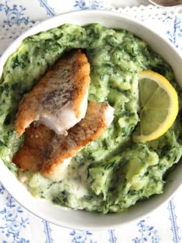 spinach potato mash served with fish fillets and lemon slices.