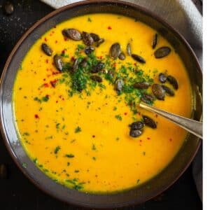 vegan roasted pumpkin soup garnished with pepitas and with a spoon in it.
