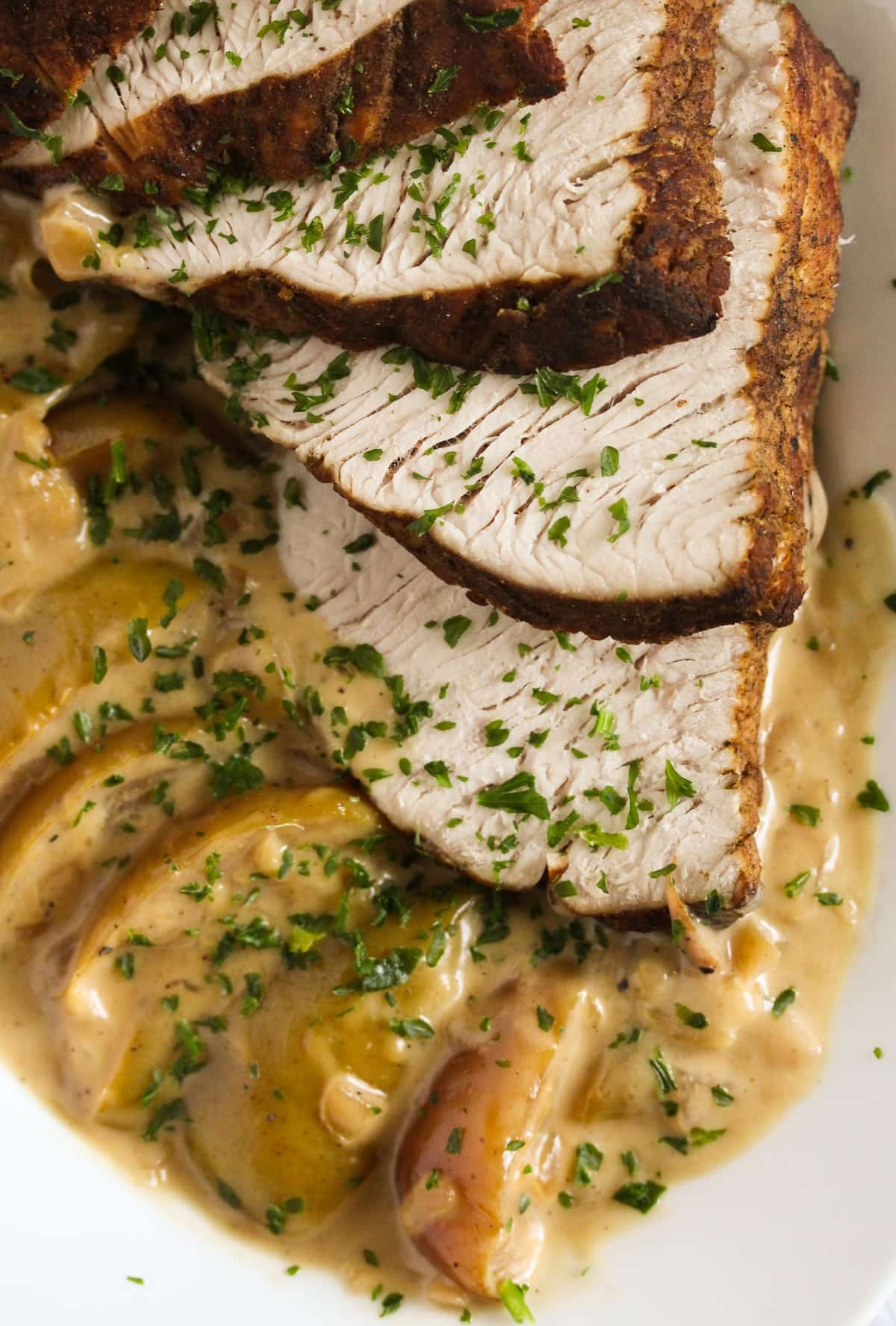 slices of turkey breast on a bed of apples with cream sauce.