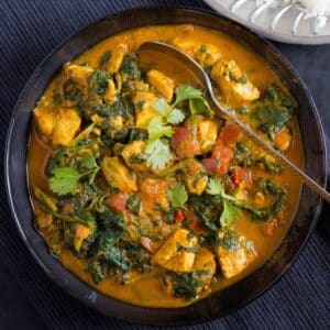 a bowl of healty chicken and spinach curry with a spoon in it on a black table cloth.