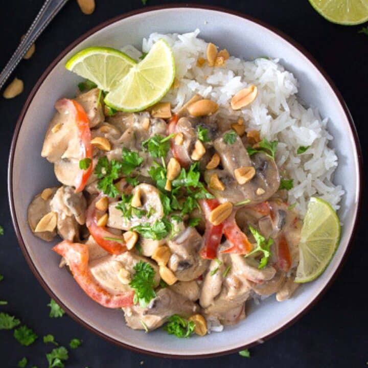 bowl of peanut butter chicken curry served with limes and rice