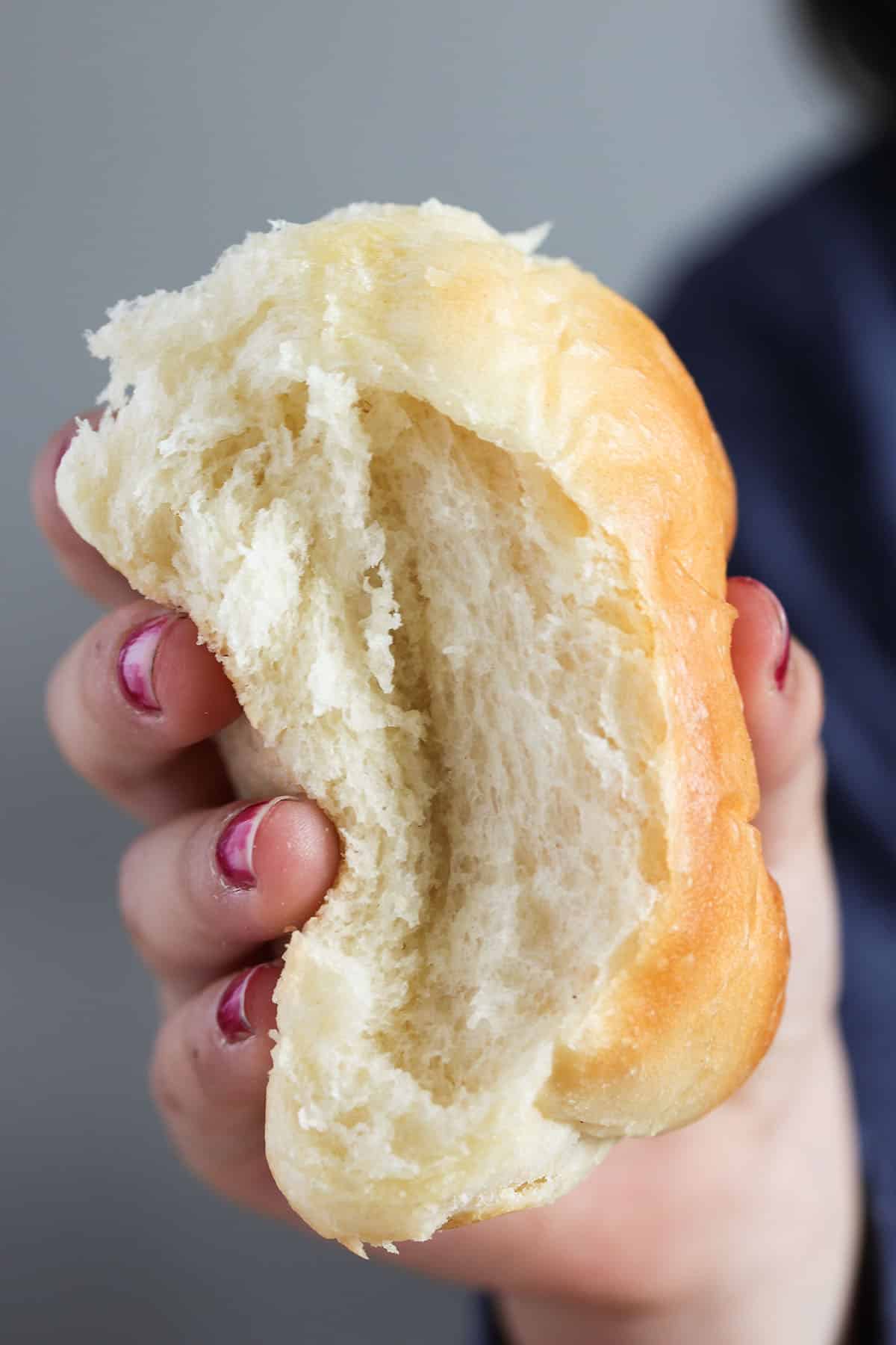 a girl's hand squeezing a yeast roll to show how fluffy it is.