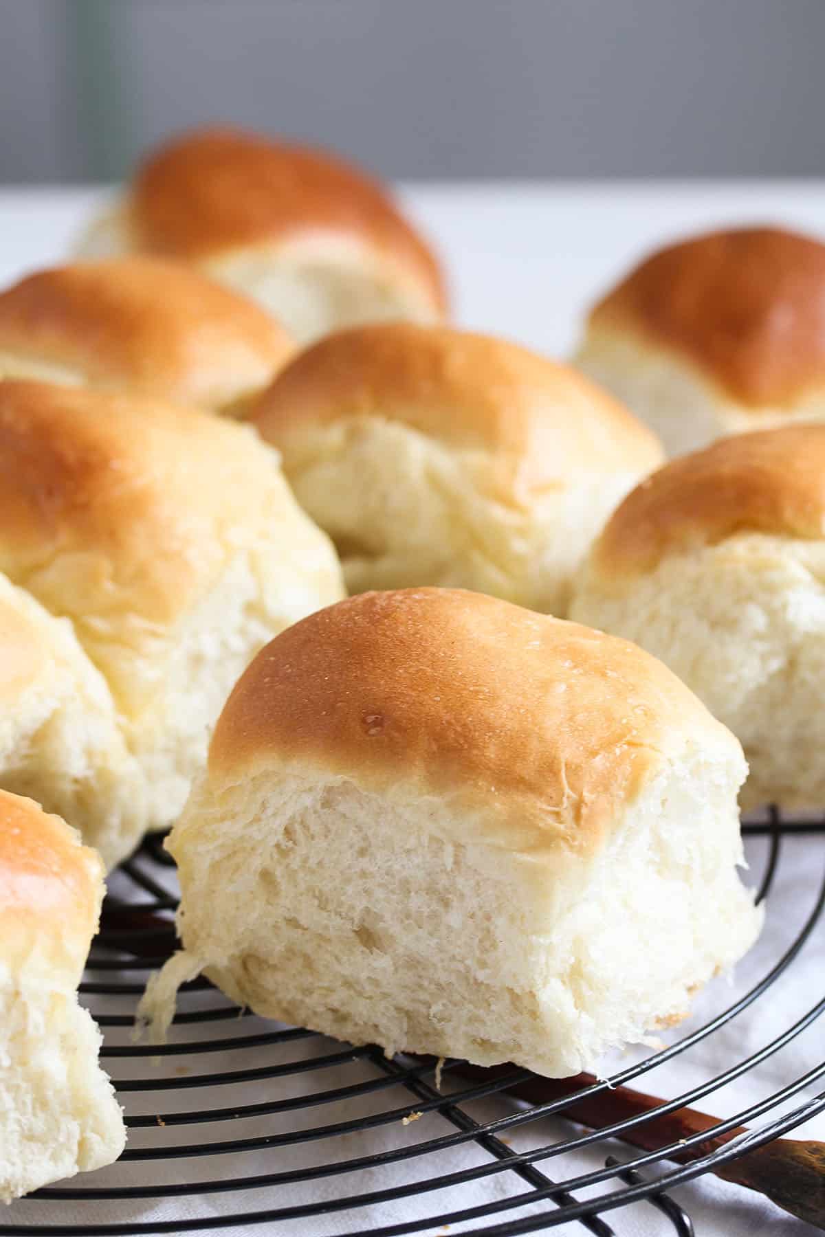 many fluffy yeast bread rolls on a wire rack.