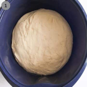 ball of yeast dough for making bread rolls in a blue bowl.