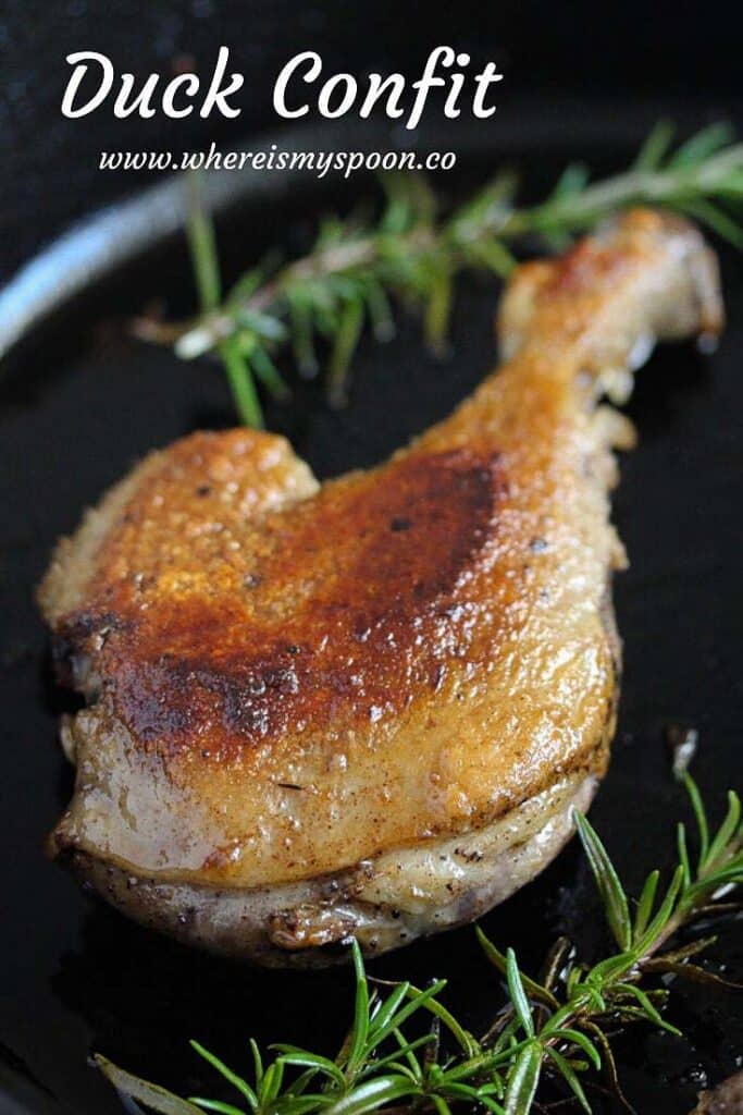 one fried duck leg confit in a pan with rosemary