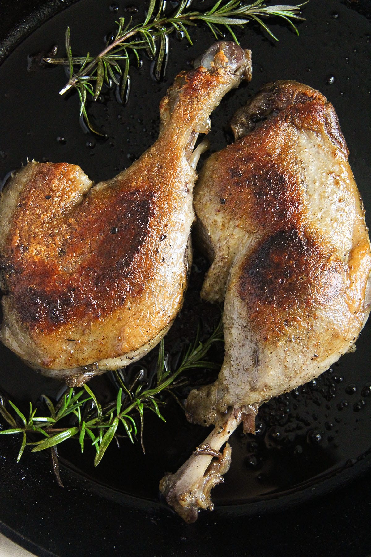 two cripsy and golden confit duck legs and rosemary sprigs.