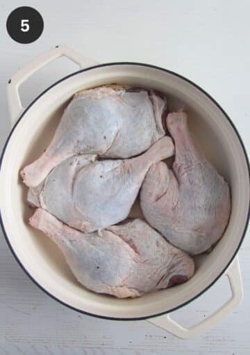 four raw duck legs tucked in a large dutch oven.