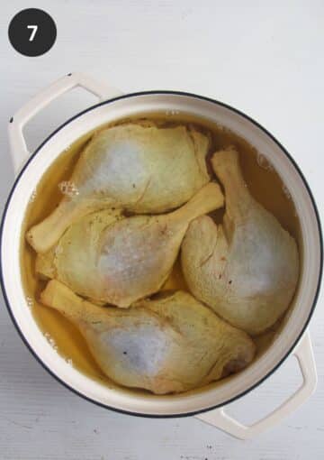 four raw duck legs covered with melted fat in a pot.