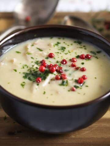 cream of turkey soup garnished with red peppercorns in a small brown bowl.