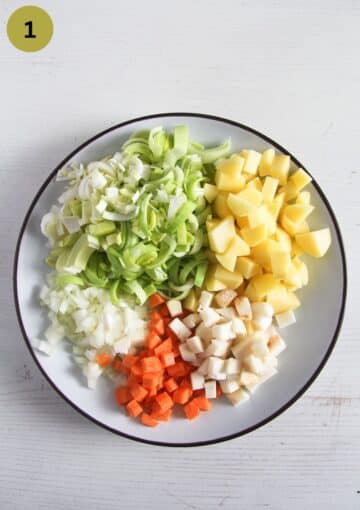 chopped leeks, potatoes, carrots, onion and celeriac on a large white plate.