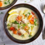 a bowl of fish soup with vegetables and pollock fillets with 2 lemon slices inside it.
