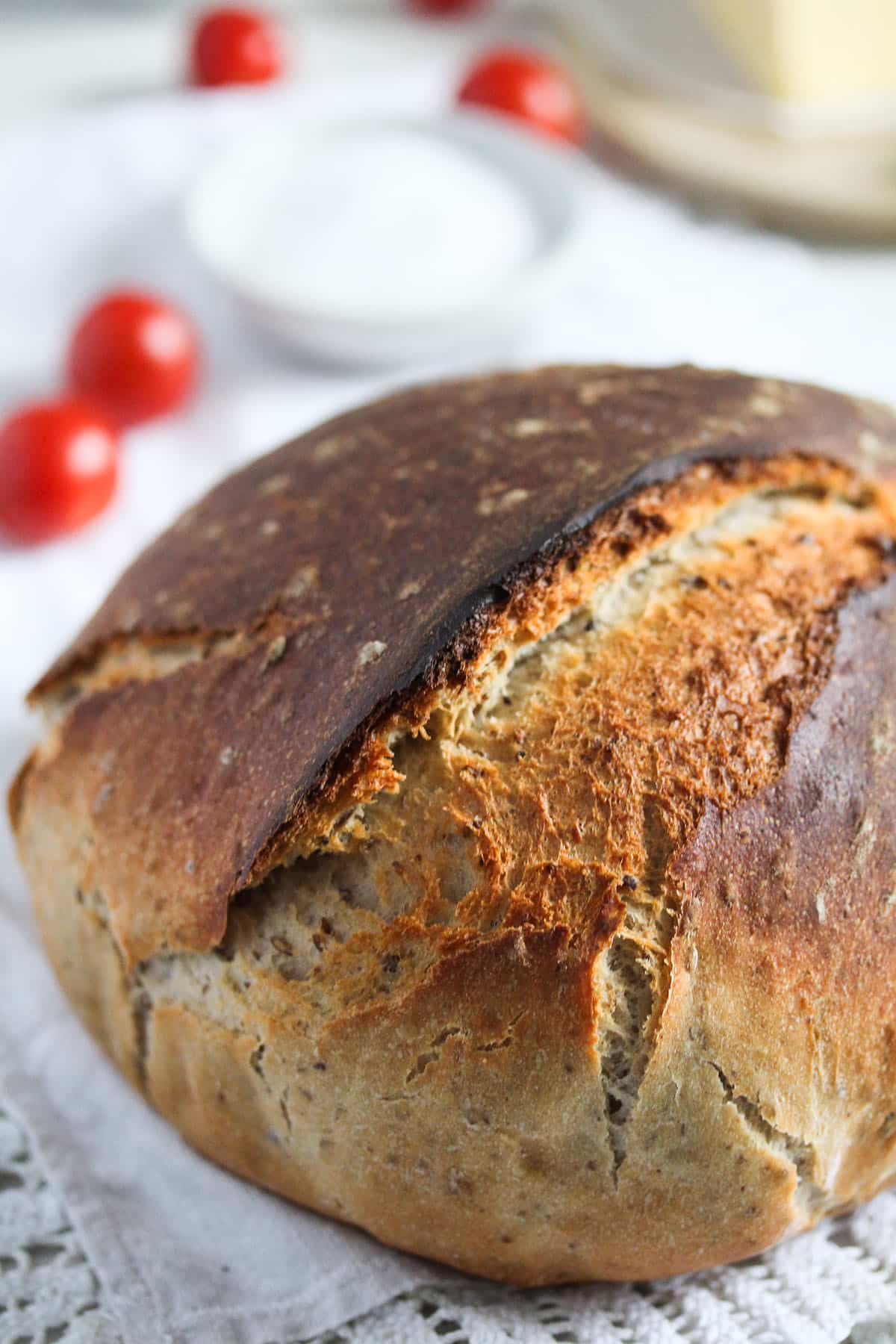 round, crusty and brown bread with some cherry tomatoes and a bowl of salt behind it.