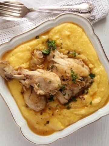 creamy polenta chicken in a square vintage serving dish with silver spoon and fork on the side.