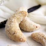 two vanillekipferl and a vanilla pod on a white cloth on the table.