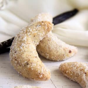 two vanillekipferl and a vanilla pod on a white cloth on the table.