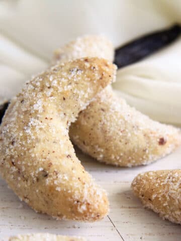 two vanillekipferl and a vanilla pod on a white cloth on the table.