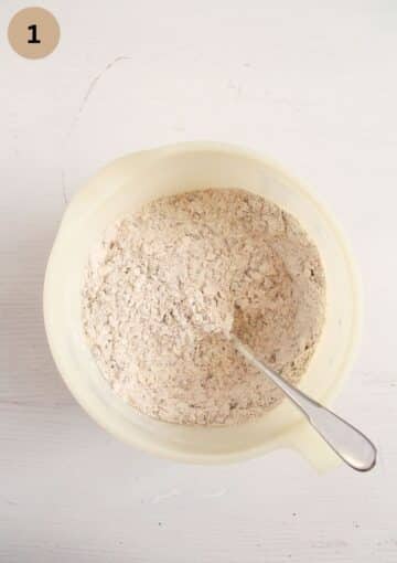 stirring dry ingredients for making bread with a spoon in a bowl.