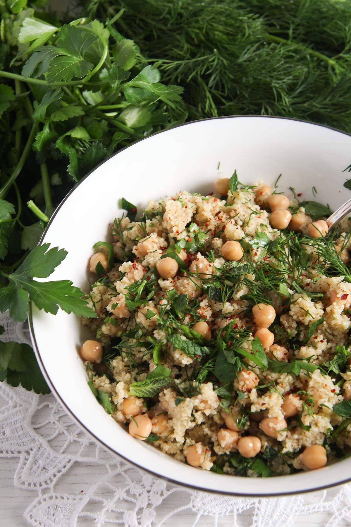 white bowl with salad with chickpeas, bulgur wheat and fresh herbs behind the bowl.