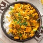 cauliflower potato curry served over rice in a brown bowl.