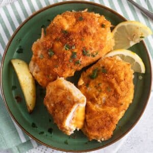 cordon bleu schnitzel on a greed plate served with lemon slices.
