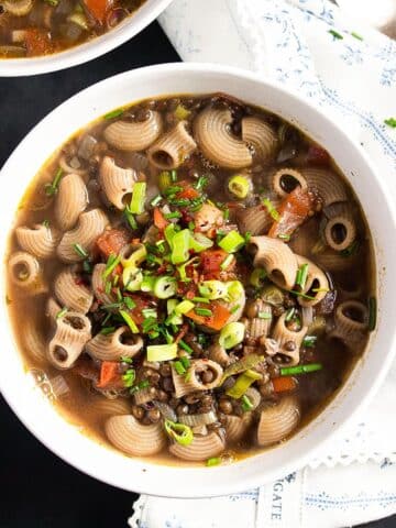 bowl of lentil pasta soup topped with green onions and tomatoes.