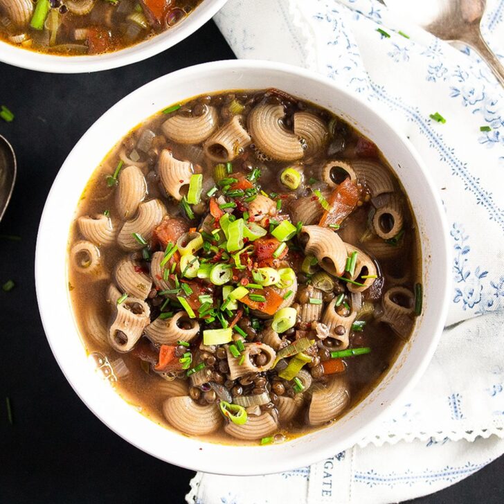 bowl of lentil pasta soup topped with green onions and tomatoes.
