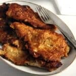 many brown pancake-battered chicken breast pieces and a fork on a platter.